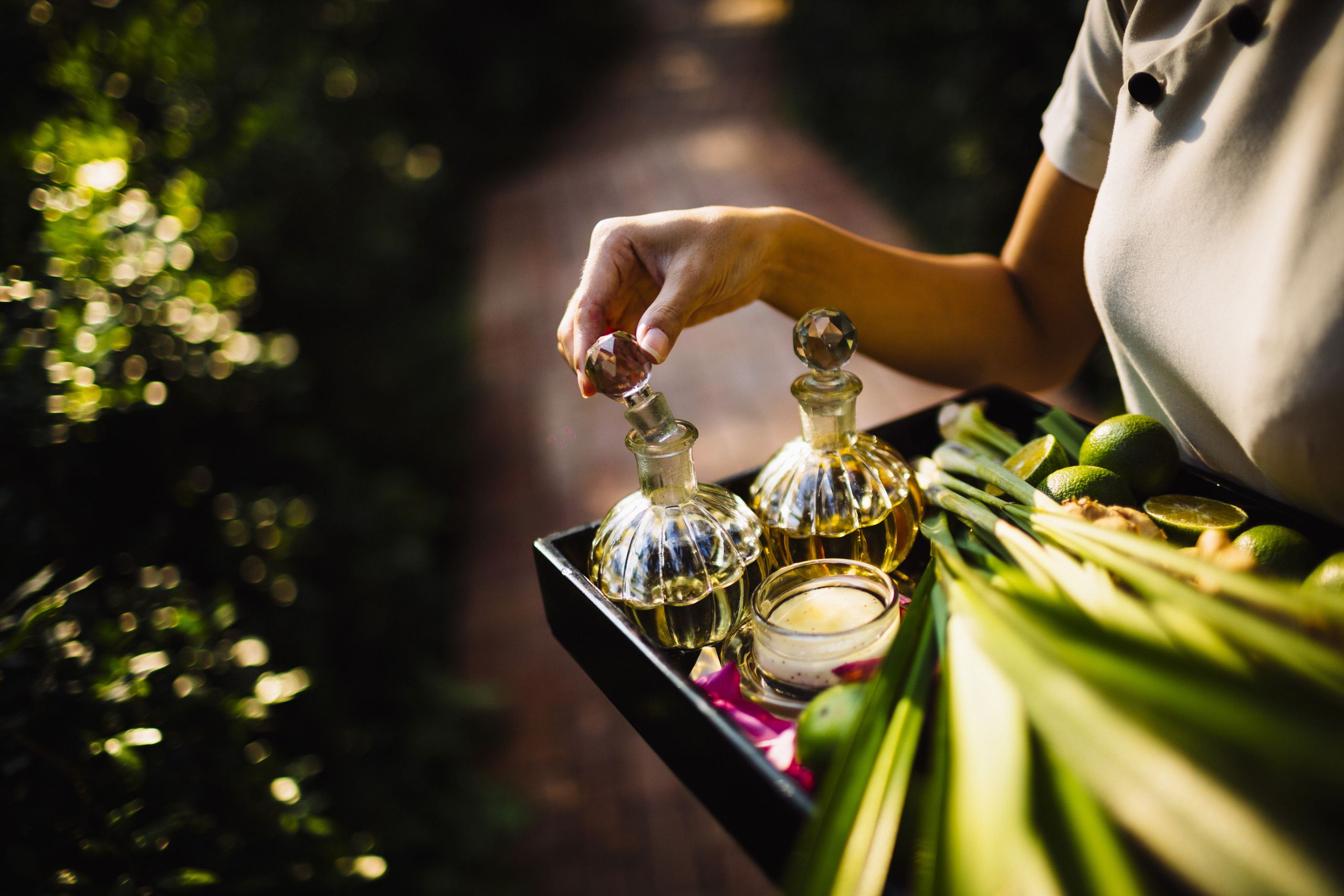 High angle close up of woman holding tray with glass bottles, candles and fruit.